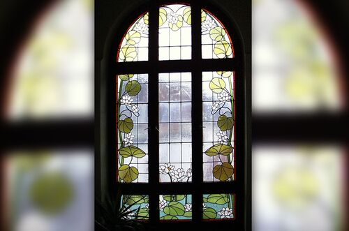 Buntes Treppenhausfenster mit floralen Motiven und Lichtdurchlässigkeit, das eine elegante Atmosphäre schafft.