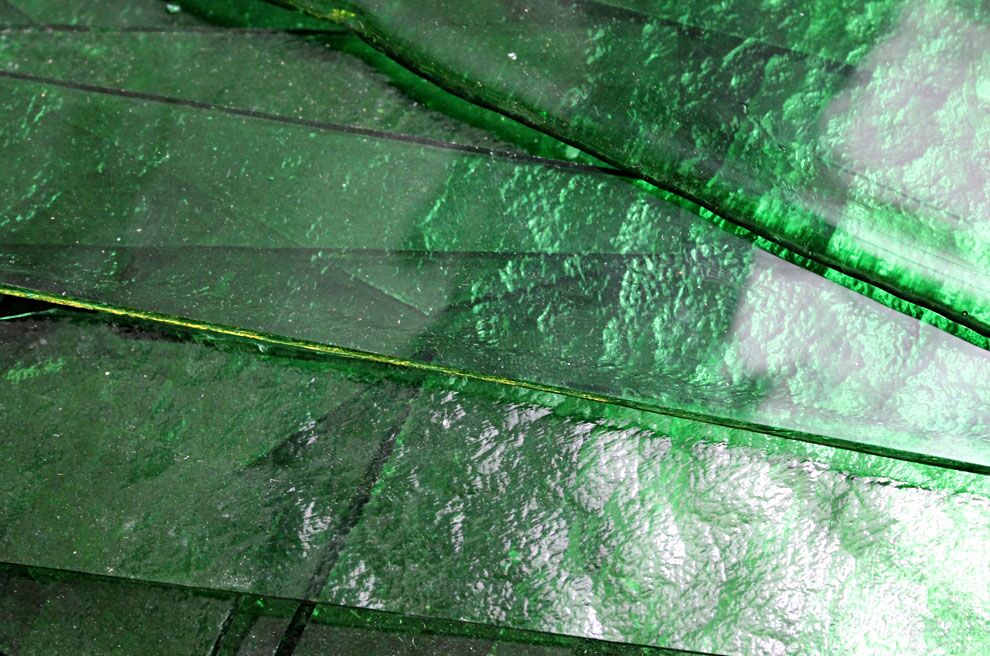 Grüne Glasscheiben liegen übereinander und reflektieren das Licht in verschiedenen Schattierungen.