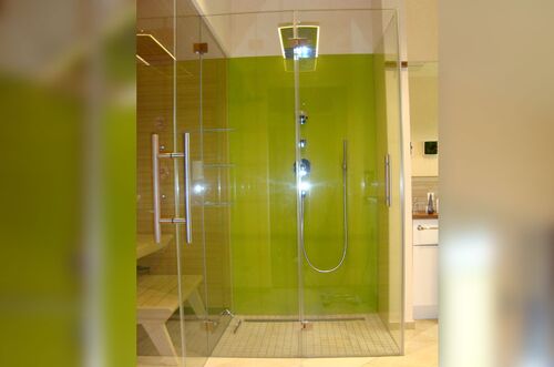Moderne Dusche mit glasklaren Wänden und leuchtend grüner Rückwand in einem stilvollen Badezimmer.