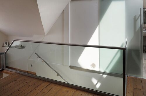 Heller Treppenaufgang mit Glasgeländer und Holzfußboden in einem modern gestalteten Dachausbau.