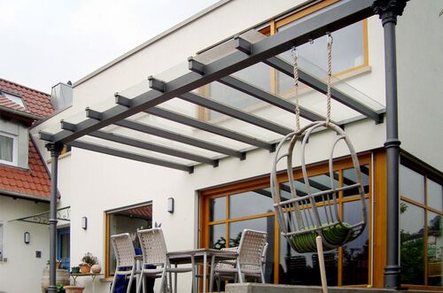 Eine moderne Terrassenüberdachung mit einem Hängesessel und Gartenmöbeln an einem hellen Tag.