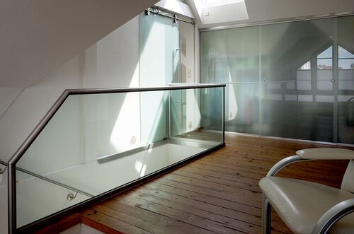 Heller Treppenaufgang mit Glasgeländer und Stuhl im Dachausbau, der Licht von einem Oberlicht empfängt.