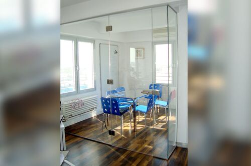 Ein moderner Raumabschluss mit Glaswänden um einen Essbereich mit blauen Stühlen und einem Glastisch.