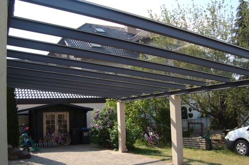 Ein moderner Carport mit Stahlträgern bietet Schatten für Fahrzeuge und Fahrräder in einem schönen Garten.