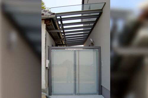 Moderner Hofeingang mit gläsernem Dach und eleganter Doppeltür aus Glas und Metall, umgeben von schlichten Wänden.
