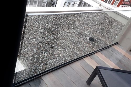 Blick auf die Terrasse mit Kies und einer modernen Glasbrüstung, die den Raum stilvoll abgrenzt.