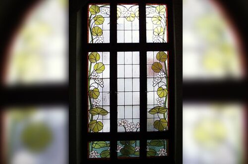 Buntes Treppenhausfenster mit floralem Design und farbigen Gläsern, das Licht kreativ filtert.