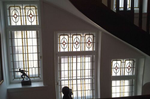 Buntglasfenster der Jugendstilvilla reflektieren Licht im Treppenhaus mit einer Statue im Vordergrund.