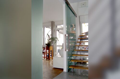 Moderne Schiebetür-Anlage und Holztreppe in einem hellen, stilvollen Innenraum mit Pflanzen und Möbeln.